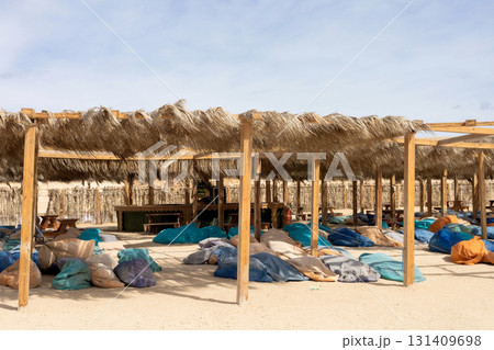 Tranquil beachside oasis with straw canopy and colorful bean bags for relaxation Tranquil beachside oasis with straw canopy and colorful bean bags for relaxation 131409698