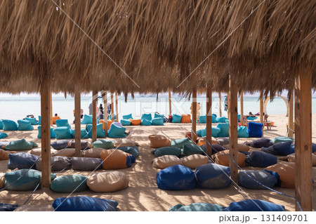 Relaxing beach lounge with colorful bean bags under straw umbrellas - ideal summer getaway 131409701