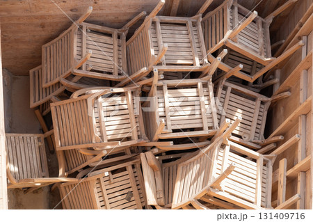 Rustic wooden chairs stacked in sunlit storage space for outdoor seating arrangement inspiration 131409716
