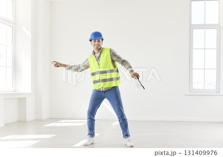 Young happy foreman working in empty new apartment wearing uniform and helmet. 131409976