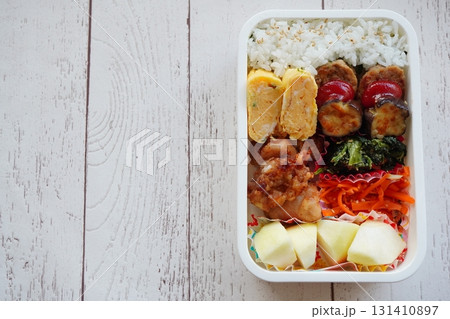 木目調のテーブルに置かれた卵焼きや唐揚げ入りの家庭的で栄養バランスに優れた健康的なお弁当写真。 131410897