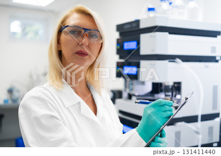 Researcher documenting the results beside liquid chromatograph HPLC . Pharmaceutical laboratory environment. Researcher documenting the results beside liquid chromatograph HPLC . Pharmaceutical laboratory environment. 131411440
