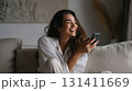 Smiling woman relaxing on sofa with smartphone, enjoying a joyful carefree moment 131411669