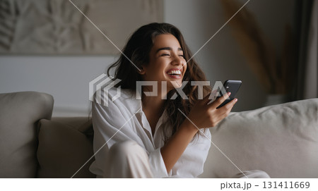 Smiling woman relaxing on sofa with smartphone, enjoying a joyful carefree moment 131411669