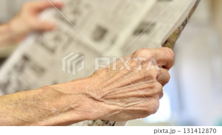 室内で新聞を持って広げる高齢者の手元_右向き 131412870