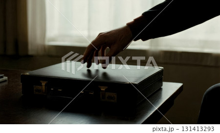 A person's hand reaching for a briefcase in a dark room. Conspiracy, secret meeting, briefcase, mystery, thriller. A person's hand reaching for a briefcase in a dark room. Conspiracy, secret meeting, briefcase, mystery, thriller. 131413293