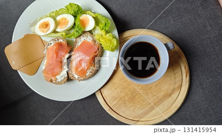 Healthy breakfast with black coffee, sandwiches with smoked salmon and cream cheese, boiled eggs, and fresh lettuce on plate Healthy breakfast with black coffee, sandwiches with smoked salmon and cream cheese, boiled eggs, and fresh lettuce on plate 131415954