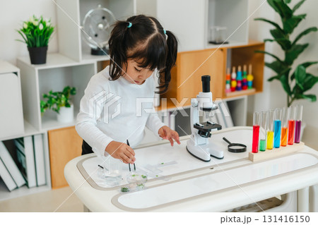 toddler girl scientist using tongs putting herbal sample in slide, preparing specimen for science microscope 131416150