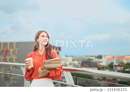 Smiling young Asian woman standing on a balcony with city view Smiling young Asian woman standing on a balcony with city view 131416172