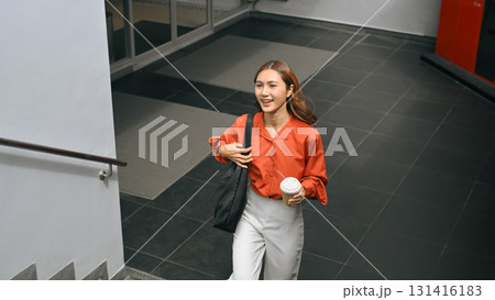 Confident woman in casual office attire holding coffee cup walking outside office building 131416183