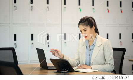 Professional businesswoman in beige suit using laptop and tablet in a modern office Professional businesswoman in beige suit using laptop and tablet in a modern office 131416184