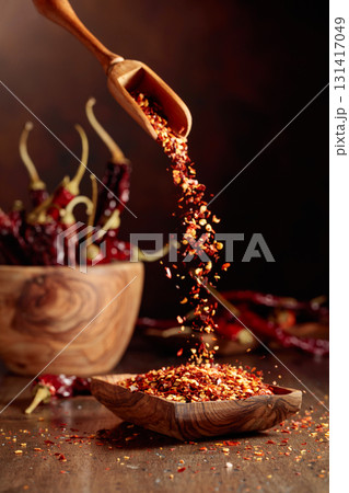 Chilli flakes are poured into a wooden dish. 131417049