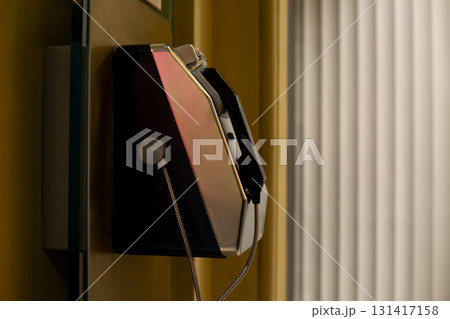 Modern public payphone mounted on wall, with unique design and metallic details. Stylish and compact, with phone cord extending from the device Modern public payphone mounted on wall, with unique design and metallic details. Stylish and compact, with phone cord extending from the device 131417158