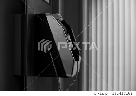 Public payphone, depicted in black and white. Sleek design of the phone and the contrast between light and shadow, emphasizing its form and functionality in minimalist, urban setting 131417162