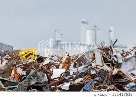 Massive concrete silos tower behind piles of scattered scrap metal and industrial debris. Scene shows impact of heavy manufacturing on fragile environment, urging sustainable waste solutions 131417632