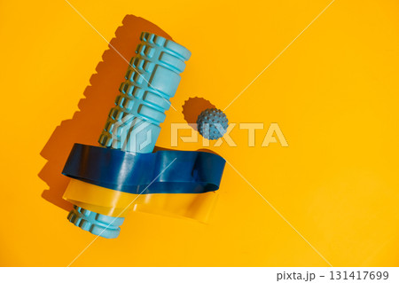 Foam roller wrapped with blue and yellow resistance bands and massage ball on yellow bold athletic recovery flat lay Foam roller wrapped with blue and yellow resistance bands and massage ball on yellow bold athletic recovery flat lay 131417699