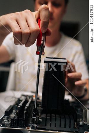 Close-up of technician installing CPU cooler onto motherboard with screwdriver, conducting maintenance and upgrades on desktop computer for improved performance and efficiency. Close-up of technician installing CPU cooler onto motherboard with screwdriver, conducting maintenance and upgrades on desktop computer for improved performance and efficiency. 131417913