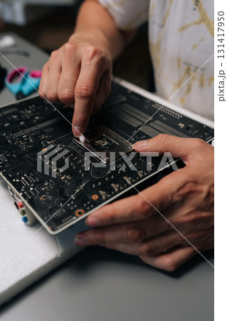 Vertical cropped shot of technician hands removing thermal paste from CPU of computer motherboard, demonstrating process of computer maintenance and repair. Concept of desktop maintenance and service. 131417950