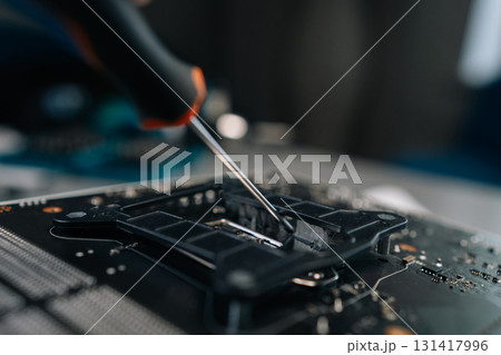 Skilled technician carefully removing aged thermal paste from computer motherboard CPU socket, readying precise surface for processor replacement. Concept of desktop PC maintenance and service. Skilled technician carefully removing aged thermal paste from computer motherboard CPU socket, readying precise surface for processor replacement. Concept of desktop PC maintenance and service. 131417996
