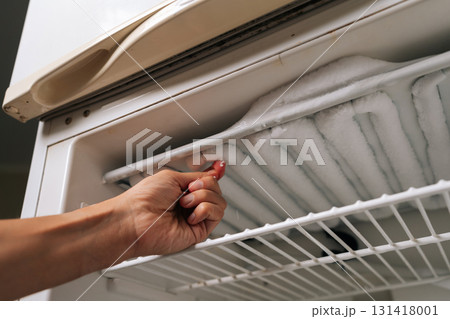 Low-angle view of housekeeper removing ice buildup from freezer compartment of refrigerator, highlighting need for regular defrosting and cleaning to maintain optimal appliance performance. 131418001