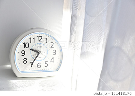 白いカーテンと目覚まし時計が映す、寝坊気味な朝の柔らかな光の写真 131418176