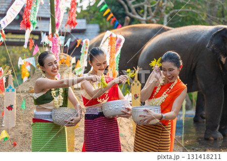 Songkran festival. Northern Thai people in Traditional clothes dressing splashing water together in Songkran day cultural festival with sand pagoda and colorful paper flag. 131418211