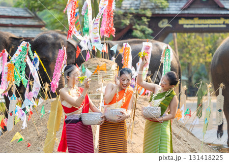Songkran festival. Northern Thai people in Traditional clothes dressing splashing water together in Songkran day cultural festival with sand pagoda and colorful paper flag. 131418225