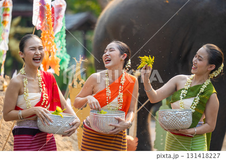 Songkran festival. Northern Thai people in Traditional clothes dressing splashing water together in Songkran day cultural festival with sand pagoda and colorful paper flag. 131418227