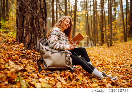 Curly-haired woman in a stylish sweater with a book sits under a maple tree. Concept of autumn. Curly-haired woman in a stylish sweater with a book sits under a maple tree. Concept of autumn. 131418725