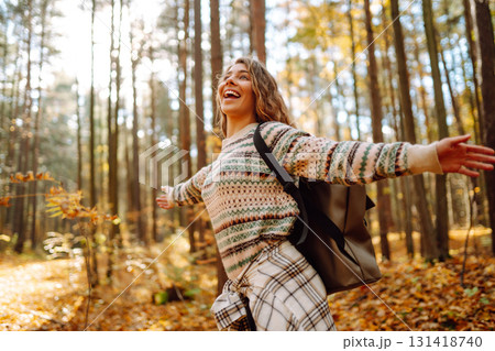 Beautiful young tourist with a backpack is having fun in the autumn forest, throwing fallen leaves. Beautiful young tourist with a backpack is having fun in the autumn forest, throwing fallen leaves. 131418740
