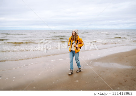 A beautiful young tourist woman in a yellow jacket with a backpack enjoys life near the sea. Travel. 131418962