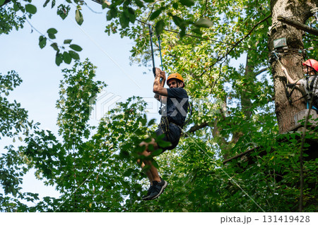 Man riding zipline through green forest in adventure park 131419428