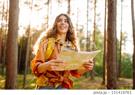A traveler woman stands in a lush forest, examining a map with a focused expression A traveler woman stands in a lush forest, examining a map with a focused expression 131419761