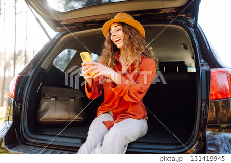 Beautiful woman sits in the trunk of a car outdoor and uses a smartphone. Active life. Beautiful woman sits in the trunk of a car outdoor and uses a smartphone. Active life. 131419945
