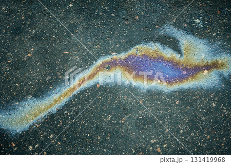 Polluting oil stain on dark asphalt creating iridescent rainbow colors, showing environmental issue Polluting oil stain on dark asphalt creating iridescent rainbow colors, showing environmental issue 131419968