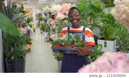 Young florist woman holding a tray of small plants smiling at the camera Young florist woman holding a tray of small plants smiling at the camera 131420004