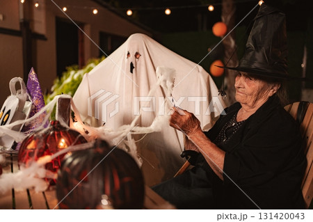 Elderly woman decorating for Halloween with a ghost costume Elderly woman decorating for Halloween with a ghost costume 131420043