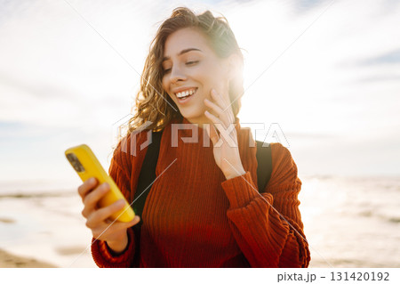 Young woman using mobile phone at beach. Cold weather. Autumn. Blogging, communication Young woman using mobile phone at beach. Cold weather. Autumn. Blogging, communication 131420192