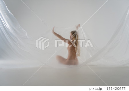 Blonde woman poses gracefully with sheer fabric in a studio setting Blonde woman poses gracefully with sheer fabric in a studio setting 131420675