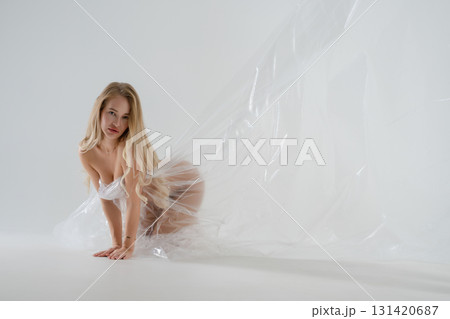 Blonde woman in a beauty studio poses gracefully with transparent fabric Blonde woman in a beauty studio poses gracefully with transparent fabric 131420687