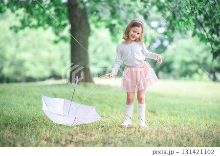 Little girl spinning with arms wide near an umbrella on the ground. A dreamy and natural moment of freedom and imaginative play in the rain. Little girl spinning with arms wide near an umbrella on the ground. A dreamy and natural moment of freedom and imaginative play in the rain. 131421102