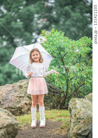 Little girl smiling and holding out her hands to catch raindrops while standing under an umbrella. Joyful exploration of weather and sensory experience in early childhood. Little girl smiling and holding out her hands to catch raindrops while standing under an umbrella. Joyful exploration of weather and sensory experience in early childhood. 131421105