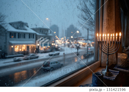 A full menorah stands by a window with an evening view of the city. The candles in the menorah burn for the Jewish holiday of Hanukkah. 131421596