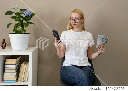 Smart woman holding smartphone and money indoors 131422001