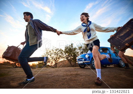 Happy couple holding hands and running with suitcases by retro blue car 131422021