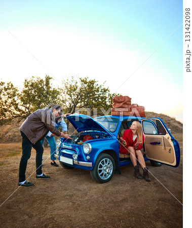Friends with retro blue car fixing engine while young woman waits with smile 131422098