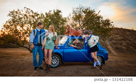 Group of young friends with luggage standing by blue retro car at sunset Group of young friends with luggage standing by blue retro car at sunset 131422108