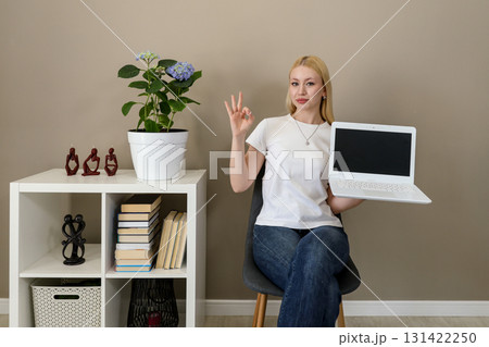 Confident woman showing OK gesture and blank laptop screen 131422250