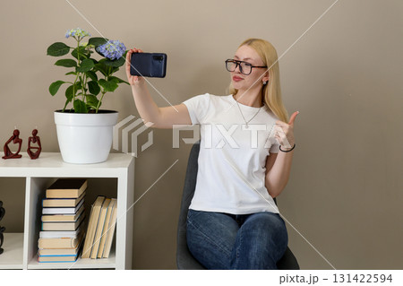 Woman taking selfie and showing thumbs up at home 131422594