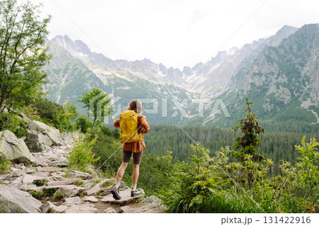 Smiling traveler with a bright backpack on a hiking mountain trail. Active lifestyle. 131422916